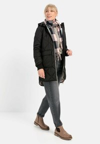 Schwarze Steppjacke mit Kapuze, grauer Pullover, kariertes Tuch in Rosa und Marineblau, graue Jeans und braune Stiefeletten mit elastischen Seiten.