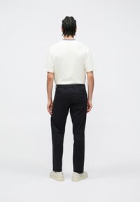 Kortærmet cremefarvet t-shirt med ribbet krave, kombineret med sorte bukser og beige sneakers. Enkel design uden synlige mønstre.