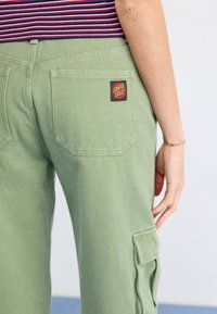 Groene cargo-broek van een gestructureerde stof, met een gestikt achterzak en een rood en geel "Santa Cruz" logo patch.
