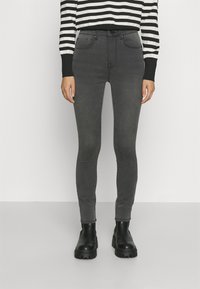 Jeans skinny grises confeccionados en una tela elástica, con un diseño clásico de cinco bolsillos y una cintura alta, combinados con botas de tobillo negras y gruesas.