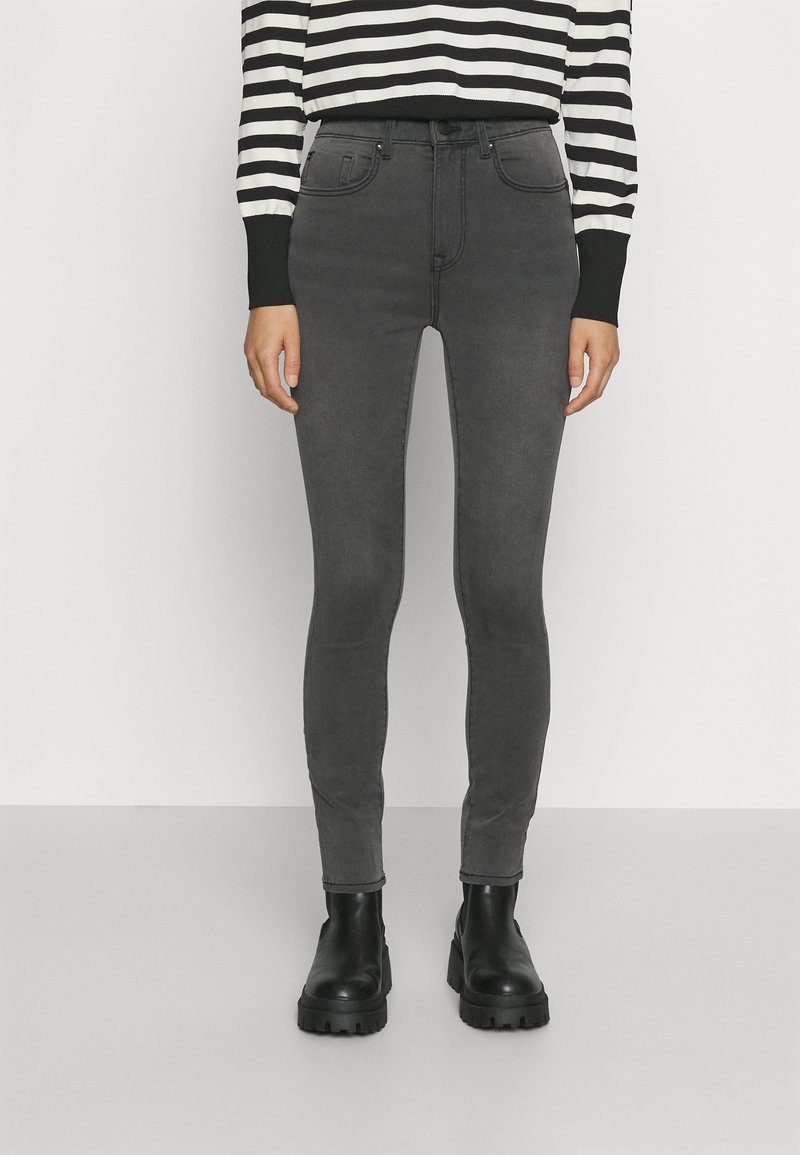 Jeans skinny grises confeccionados en una tela elástica, con un diseño clásico de cinco bolsillos y una cintura alta, combinados con botas de tobillo negras y gruesas.