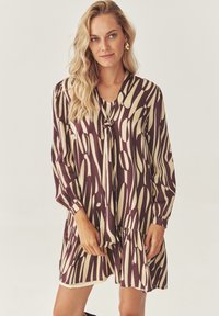 Robe courte marron et crème avec un motif abstrait. Dot�ée de manches longues, d'un décolleté en V et d'un ourlet froncé. Texture de tissu lisse.