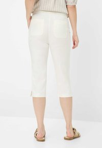 Pantalons blancs courts avec poches arrière, texture lisse et ourlets fendus, associés à des sandales beiges au design de lanière simple.