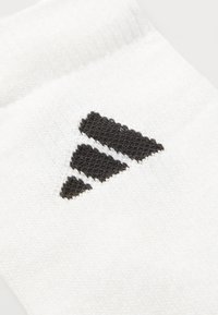 Nahaufnahme einer weißen Socke mit einem schwarzen Drei-Streifen-Logo, das nahe dem oberen Rand eingestrickt ist.