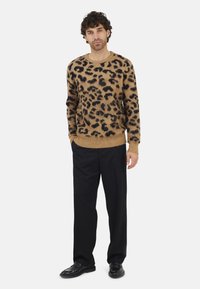 Pull en imprimé léopard beige et noir, en matière douce, avec un col rond et des poignets côtelés, associé à un pantalon noir.