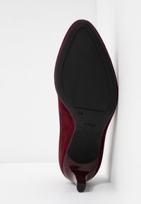 Burgundy mockasins med hög klack och spetsig tå, svart gummisula och en subtil glans på klacken. Störrelse märkt som 4½.