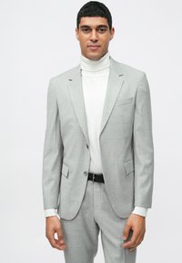 Fato ajustado cinza-claro com um padrão xadrez subtil, combinado com um pulôver branco. Apresenta lapelas em bico e bolsos laterais. Cinto preto visível.