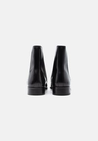Ghete de gleznă din piele neagră cu textură netedă, panouri laterale elastice și toc mic suprapus. Detaliile cusăturii accentuează silueta.