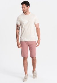 Světle krémové tričko s mramorovým vzorem, doplněné jemně růžovými šortkami. Pohodlný a uvolněný design, doplněný béžovými teniskami.