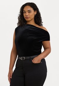 Svart sammetstopp med en axel, med mjuk textur och samlad tygdetalj. Matchas med högmidjade svarta byxor och ett bälte med silverspänne.