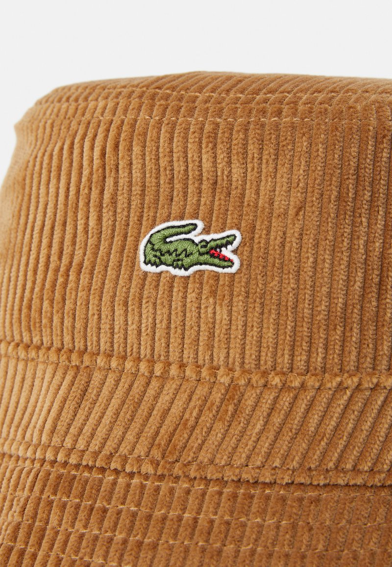 Cappello a secchiello in velluto a coste marrone con righe verticali, con un logo di coccodrillo ricamato in verde e rosso sulla parte frontale.
