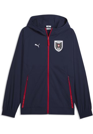 Marineblaue Kapuzenjacke mit rotem Reißverschluss und Taschenumschlägen, Puma-Logo auf der rechten Brust und schwarz-weiß-rotem Wappen mit Fußb all auf der linken Brust.