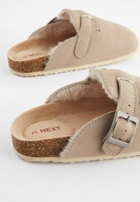 Beiga slip-ons med mjukt foder av päls, överdel i läder och justerbart spänne. Korkliknande sula och strukturerad innersula för komfort.