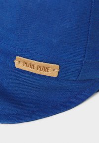 Blå lerret caps med en teksturert overflate og en lærlabel merket "PURE PURE," sydd sikkert til skjermen.