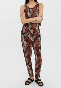 Jumpsuit à motif floral avec un design sans manches, mettant en valeur des motifs de feuilles rouges et bleues sur un fond clair, une taille élastique et des jambes fuselées.