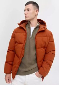 Orange padded jacket with a hood, featuring a full zipper and ribbed cuffs. Worn over a knitted, olive green sweater.