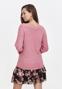 Różowy sweter z dzianiny o szerokim dekolcie, długich rękawach i prążkowanym wykończeniu, zestawiony z czarną spódnicą w kwiaty z falbankami, zdobioną różowymi kwiatami.