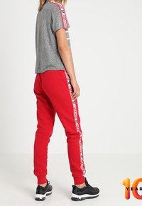 Grijze T-shirt met korte mouwen en rode accenten, gecombineerd met rode joggingbroek met witte zijstrepen en zwarte sportschoenen.