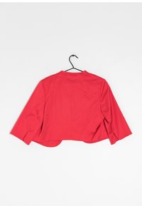 Veste rouge courte avec des manches trois-quarts, un col plat, une texture lisse et des fentes sur les côtés, accrochée à un crochet noir sur fond blanc.