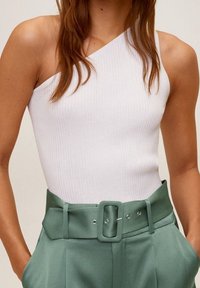 Débardeur blanc côtel é avec un col asymétrique, associé à un pantalon taille haute vert menthe avec une large ceinture et une boucle rectangulaire.