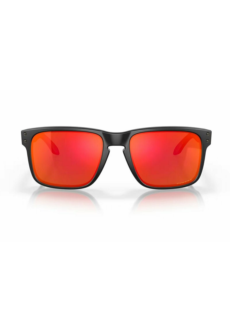Lunettes de soleil noires rectangulaires avec des verres miroités rouges. Elles présentent une monture en plastique robuste avec des charnières visibles et des accents métalliques subtils.