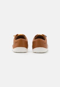 Scarpe in pelle marrone con design arrotondato, suole in gomma bianche e dettagli colorati sul tallone. Stile pulito e minimalista visto da dietro.