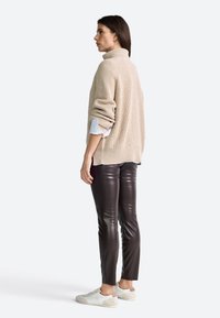 Maglione beige lavorato a maglia con colletto alto, abbinato a leggings in pelle marrone e sneakers bianche con dettagli marrone chiaro.