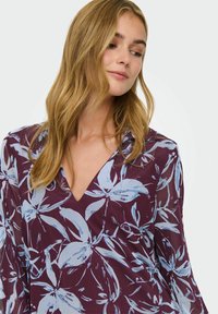 Kerge kangast lilleline pluus tumepunases toonis, sinise lillemustriga, V-kaelusega ja pikkade varrukatega.