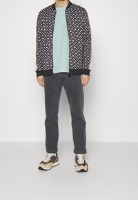 Bavlněná bomber bunda s námořnickým vzorem a geometrickými designy, světle modré tričko, šedé džíny a multicolor tenisky. Texturovaná tkanina, žebrované manžety.