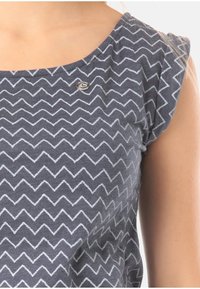 Tmavě modré tričko s chevronovým vzorem v světle šedé, krátkými volánovými rukávy a malým logem na levé straně.