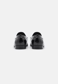 Zapatos de vestir de cuero negro con un acabado brillante, punta redondeada, tacón bajo y diseño minimalista. Tacón reforzado y textura suave.