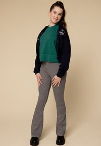 Groene cropped sweatshirt onder een marineblauwe jas met logo, gecombineerd met grijs gestreepte flare-broek en zwarte plateau-schoenen.
