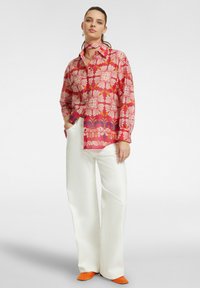 Camicia a maniche lunghe colorata con un motivo floreale rosa e bianco, abbinata a pantaloni bianchi a gamba larga e scarpe arancioni.