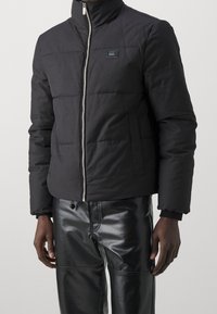 Sort oppustelig jakke med høj krave, lynlås lukning og frontlomme. Har et quiltet design og elastiske manchetter.