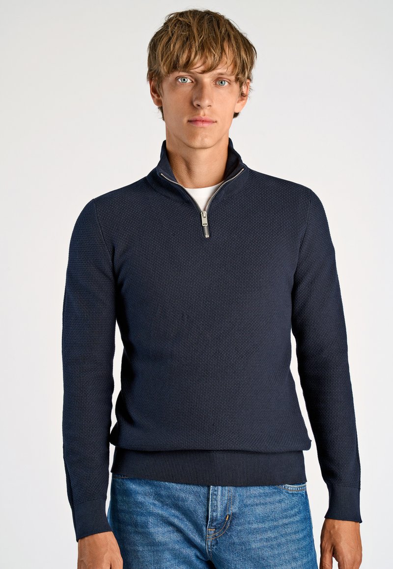Marineblauer Pullover mit hohem Kragen und Reißverschluss, der über ein strukturiertes Strickmuster sowie gerippte Bündchen und Saum verfügt.