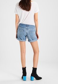 Pantalones cortos de denim azul claro con puños enrollados, bolsillos traseros, combinados con botas negras hasta el tobillo con tacones cuadrados azules. Camiseta blanca sencilla.