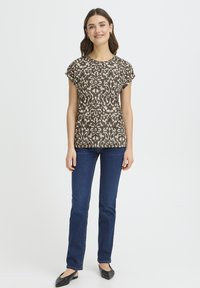 Barna mintás rövid ujjú felső kerek nyakkivágással, sötétkék farmerrel és fekete balerinacipővel párosítva. Simaságú anyag és testhezálló szabás.