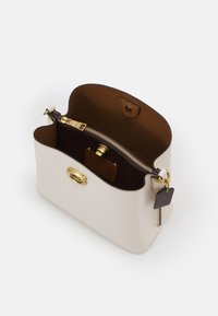 Rakennettu käsilaukku kermanvärisestä nahasta kultasävyisillä hardwareilla. Varustettu ruskealla sisätilalla, vetoketjupussilla ja koristeellisella tarralla. Silkinsileä tekstuuri, pyöristetyt reunat.