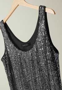 Musta tanktoppi, jossa on hopeiset paljetit järjestetty pystysuoraan. Sujuva pinta, pyöreä pääntie ja leveät olkaimet.