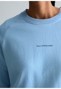 Sweat-shirt bleu clair à col rond porté par une personne, avec un petit texte en relief "Marc O'Polo DENIM" sur la poitrine.