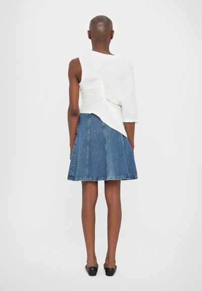 Biely asymetrický top s r gathered detailom na zadnej strane, skombinovaný s modrou džínsovou sukňou v A-strihu. Čierne baleríny doplňujú celkový vzhľad.
