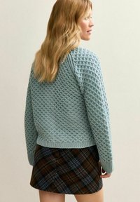 Jasnoniebieski sweter z dzianiny o strukturalnym wzorze, z ściągaczami na mankietach i u dołu. Połączony z mini spódniczką w kratę w brązowych i niebieskich odcieniach.