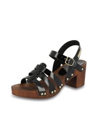 Sandal de charol negro con tacón de bloque de madera, con correas entrelazadas y tachuelas en tono dorado a lo largo de la suela. Cierre de hebilla en la correa del tobillo.