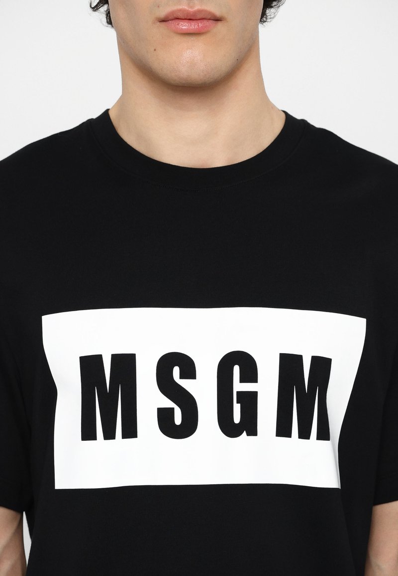 Schwarzes Baumwoll-T-Shirt mit einem auffälligen weißen rechteckigen Grafikdesign, das "MSGM" in schwarzer Schrift auf der Vorderseite zentriert. Kurze Ärmel, Rundhalsausschnitt.