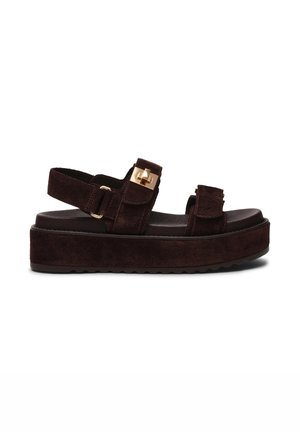 Brown suede platform sandals with two adjustable straps, gold hardware accents, and a textured sole. Chunky design with a flat footbed.
