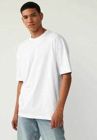 Hvid bomulds t-shirt med afslappet fit, korte ærmer og klassisk rund halsudskæring, parret med lyseblå denim jeans.