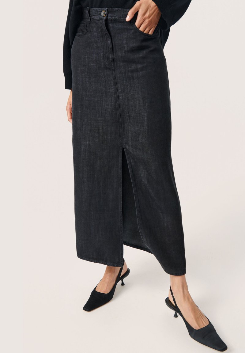 Schwarzer Denim-Midirock mit Schlitz vorne, hoher Taille und Taschen, kombiniert mit schwarzen Slingback-Absätzen. Glatte Textur.