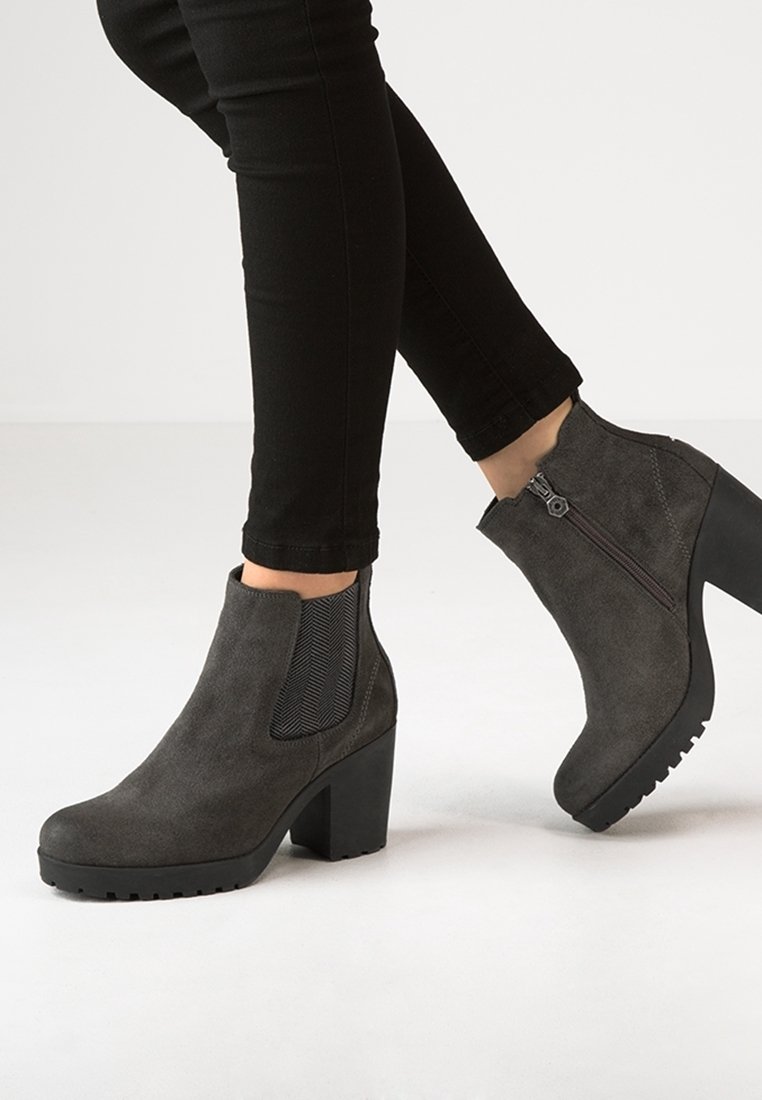 Stivaletti grigi alla caviglia con una finitura in suede testurizzata, pannelli laterali elasticizzati e un tacco spesso. Le suole nere presentano un design a tasselli per una maggiore aderenza.
