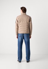 Beige puffjacka med hög krage, vadderad design och kontrasterande svarta detaljer på axlarna, bärs över blå rak benjeans.