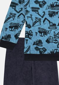 Hellblauer Fleece-Pullover mit schwarzen Druckmotiven von Baustellenfahrzeugen, kombiniert mit dunkelblauen Shorts. Der Pullover hat einen schwarzen Saum am unteren Rand und an den Ärmeln.